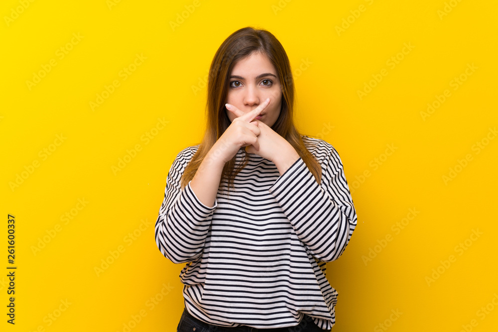 Young girl over yellow wall showing a sign of silence gesture Young girl over yellow wall showing a sign of silence gesture