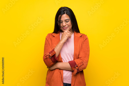 Young Colombian girl over yellow wall looking down with the hand on the chin