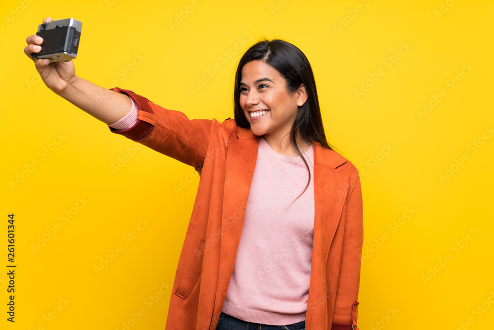 Young Colombian girl over yellow wall holding a camera Young Colombian girl over yellow wall holding a camera