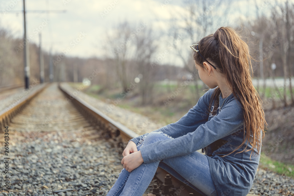 Pensive girl sitting on railway. Side view of young thoughtful girl sitting on rail and looking away in nature	