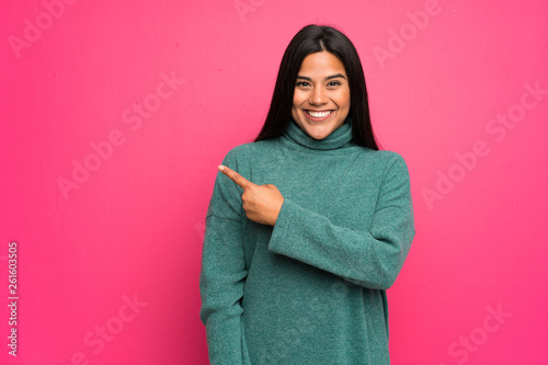 Young Colombian girl with green sweater pointing to the side to present a product © luismolinero