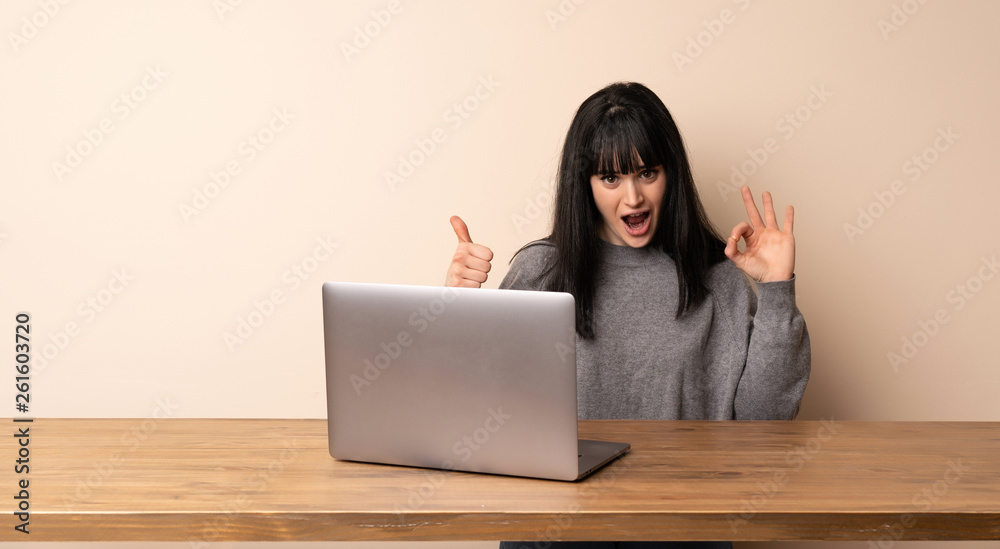 Young woman working with her laptop showing ok sign with and giving a thumb up gesture Young woman working with her laptop showing ok sign with and giving a thumb up gesture