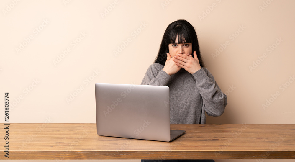 Young woman working with her laptop covering mouth with hands for saying something inappropriate