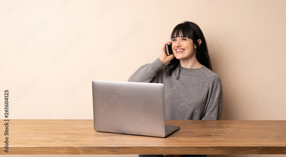 Young woman working with her laptop keeping a conversation with the mobile phone Young woman working with her laptop keeping a conversation with the mobile phone
