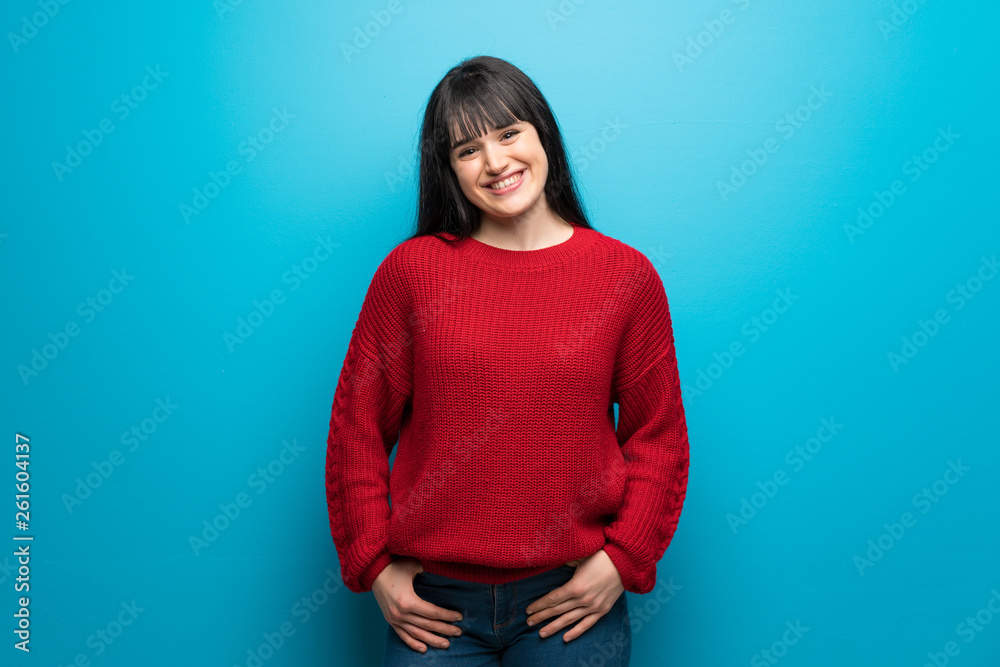 Woman with red sweater over blue wall laughing looking to the front Woman with red sweater over blue wall laughing looking to the front