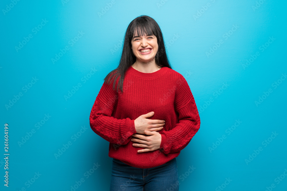 Woman with red sweater over blue wall smiling a lot