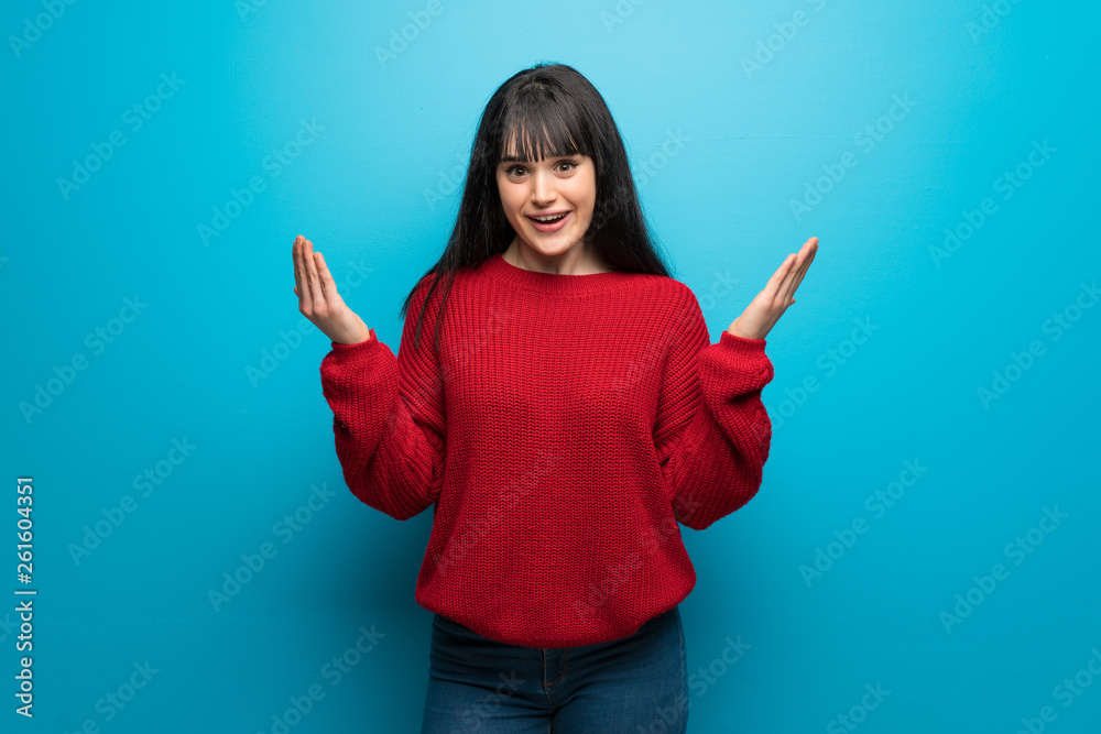 Woman with red sweater over blue wall with shocked facial expression Woman with red sweater over blue wall with shocked facial expression