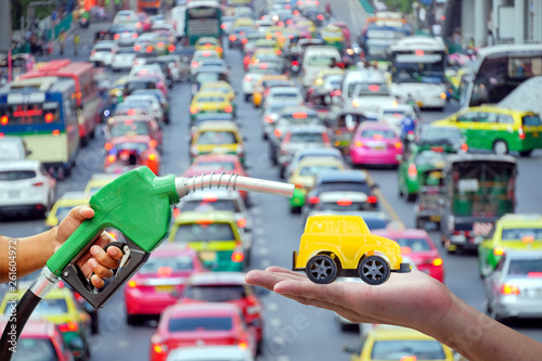 Left hands of men who were holding an automatic nozzle to make refill oil on yellow toy car on right hand with traffic jam on blurred background, industry oil and gas energy concept