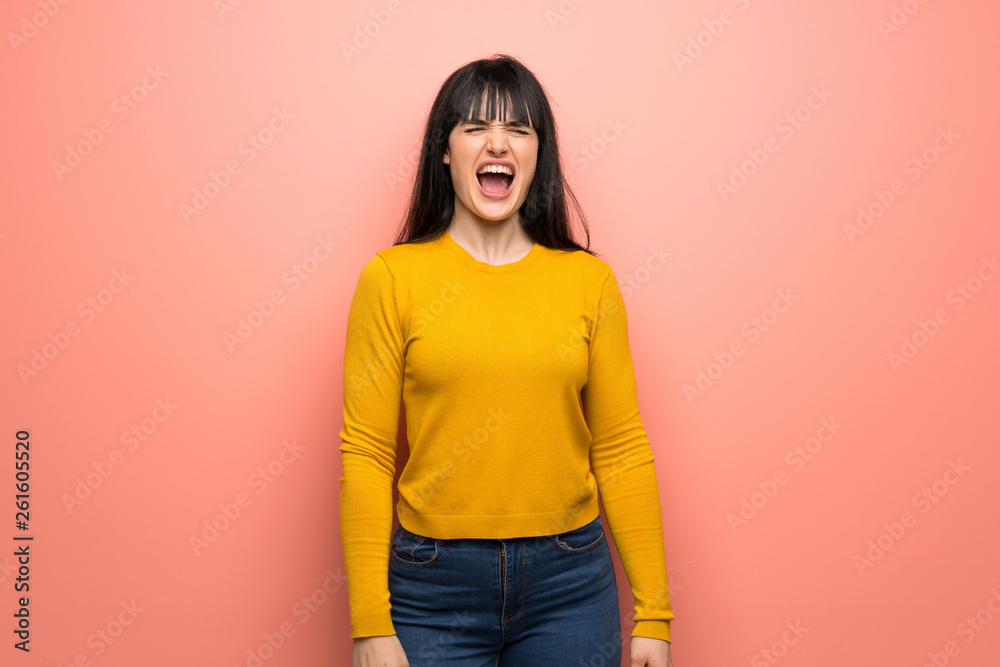 Woman with yellow sweater over pink wall shouting to the front with mouth wide open Woman with yellow sweater over pink wall shouting to the front with mouth wide open