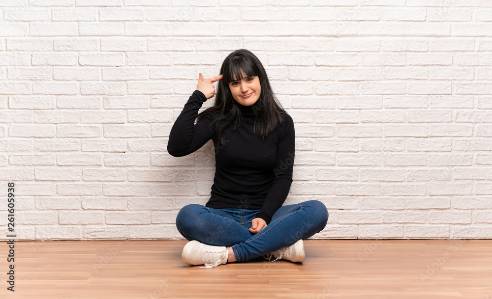 Woman sitting on the floor making the gesture of madness putting finger on the head Woman sitting on the floor making the gesture of madness putting finger on the head
