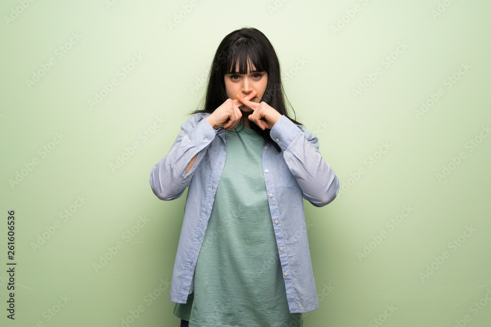Young woman over green wall showing a sign of silence gesture Young woman over green wall showing a sign of silence gesture