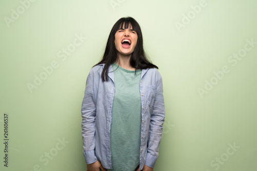 Young woman over green wall shouting to the front with mouth wide open