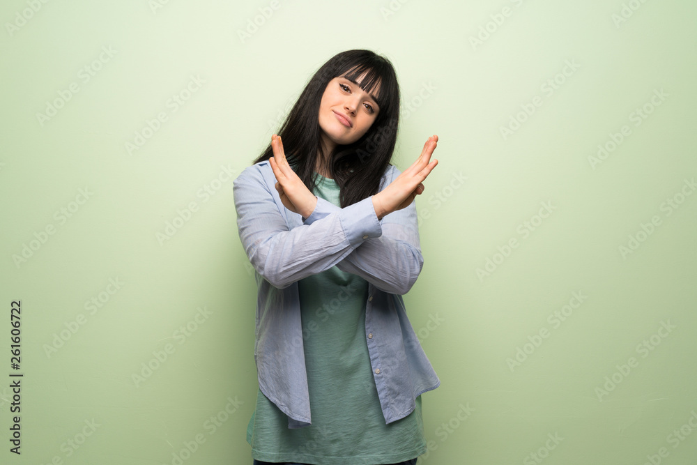 Young woman over green wall making NO gesture Young woman over green wall making NO gesture