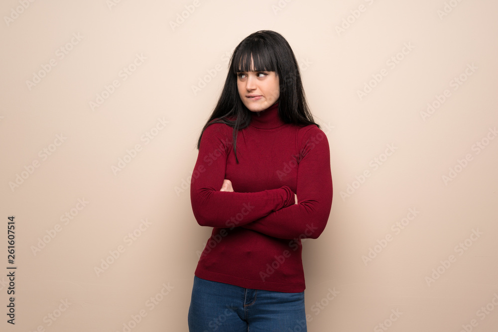 Young woman with red turtleneck with confuse face expression while bites lip Young woman with red turtleneck with confuse face expression while bites lip