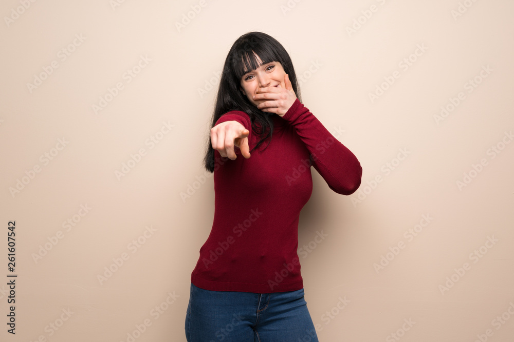 Young woman with red turtleneck pointing with finger at someone and laughing Young woman with red turtleneck pointing with finger at someone and laughing