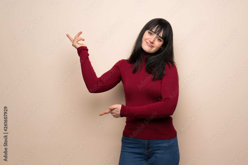 Young woman with red turtleneck extending hands to the side for inviting to come Young woman with red turtleneck extending hands to the side for inviting to come