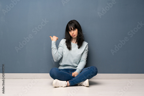 Woman sitting on the floor unhappy and pointing to the side