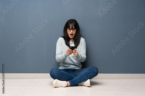 Woman sitting on the floor surprised and sending a message