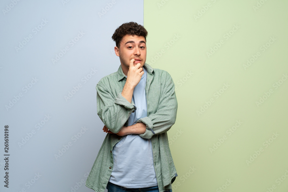 Young man over blue and green background having doubts while looking up Young man over blue and green background having doubts while looking up