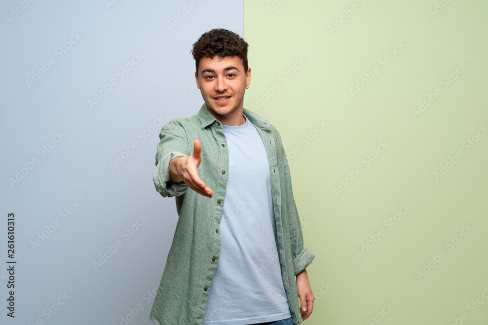 Young man over blue and green background shaking hands for closing a good deal