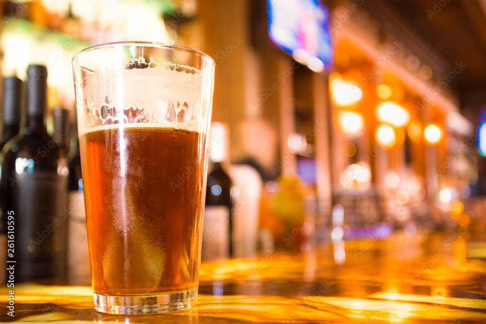 Φωτογραφία Glass Pint of amber beer with colorful blur of bar in background