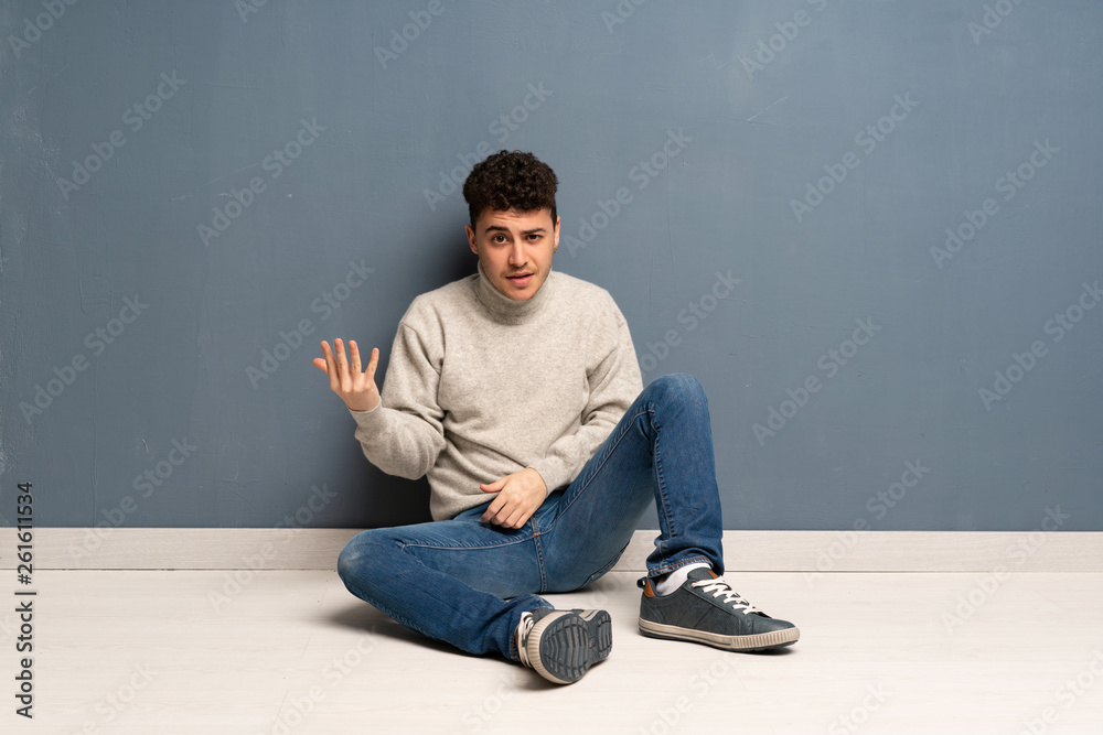 Young man sitting on the floor making doubts gesture Young man sitting on the floor making doubts gesture