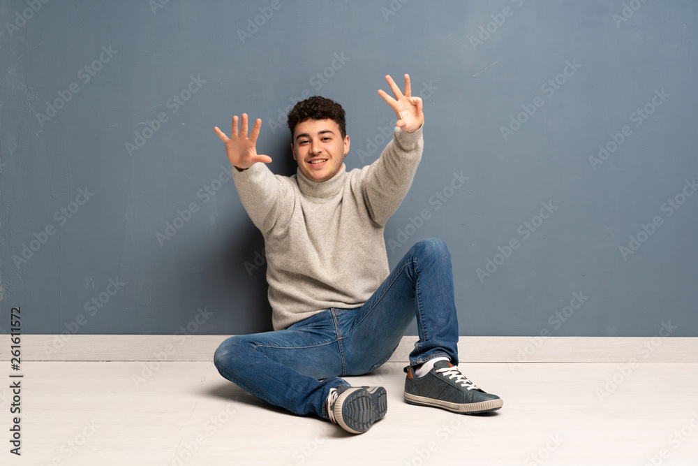 Young man sitting on the floor counting nine with fingers Young man sitting on the floor counting nine with fingers