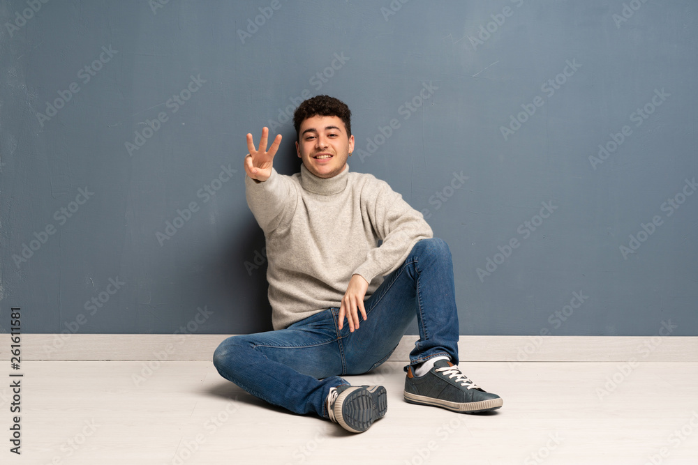 Young man sitting on the floor happy and counting three with fingers Young man sitting on the floor happy and counting three with fingers