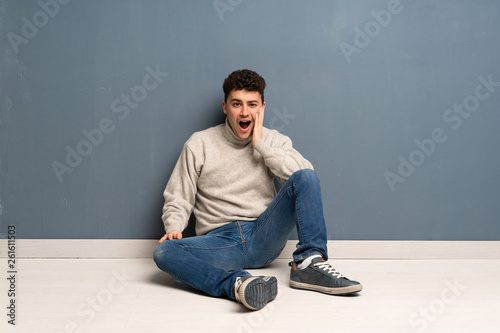 Young man sitting on the floor with surprise and shocked facial expression