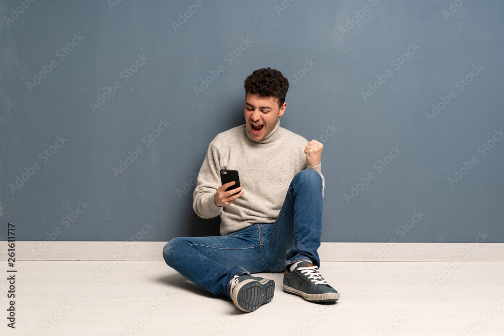 Young man sitting on the floor with phone in victory position Young man sitting on the floor with phone in victory position