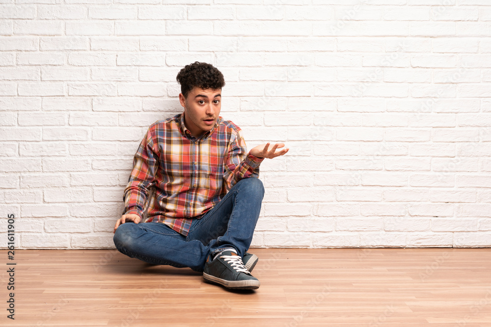 Young man sitting on the floor making doubts gesture Young man sitting on the floor making doubts gesture
