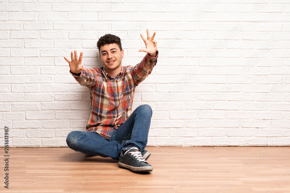 Young man sitting on the floor counting nine with fingers Young man sitting on the floor counting nine with fingers