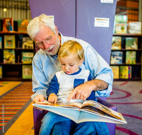 Grandfather Teaches Grandson to Read at Library