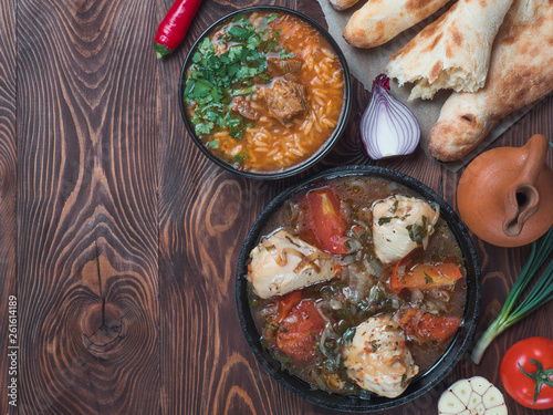 Traditional Georgian kitchen - spicy Kharcho soup and chicken Chachochbili, traditional bread Shotis Puri, vintage wine jar, fresh vegetables on wooden table. Copy space for text. Top view photo