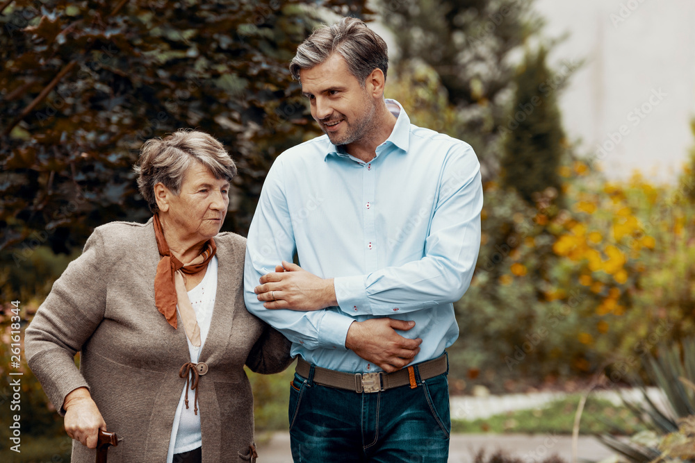 Fototapeta premium Smiling man supporting senior woman while walking in the garden