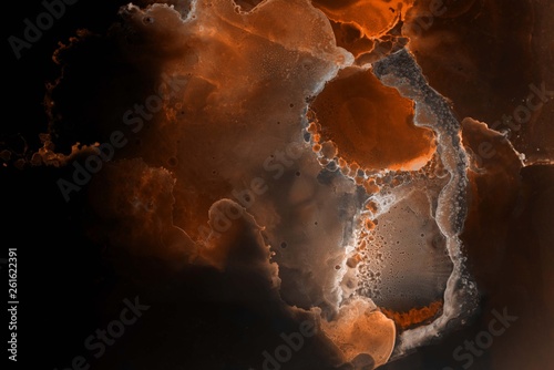 Orange alcohol ink texture with abstract washes and paint stains on the black paper background. 