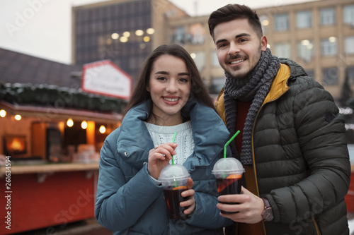 Young couple with cups of mulled wine at winter fair. Space for text