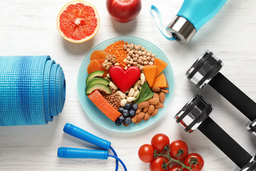 Plate with heart-healthy products and sports equipment on wooden background, flat lay