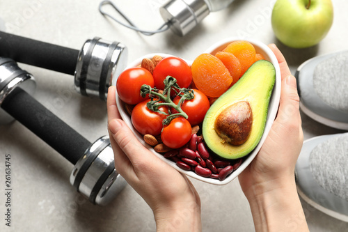 Fototapeta Naklejka Na Ścianę i Meble -  Woman holding heart-healthy products over table with sports equipment, top view