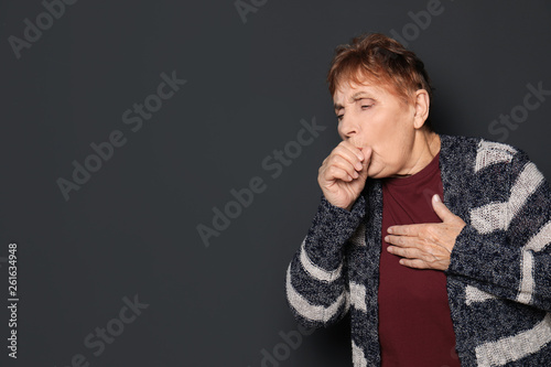 Elderly woman coughing against dark background. Space for text