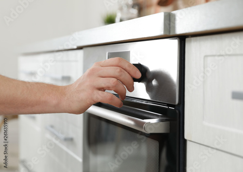 Man regulating cooking mode on oven panel in kitchen, closeup