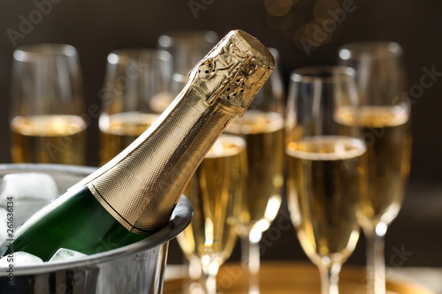 Bottle of champagne in bucket with ice and glasses on blurred background, closeup. Space for text photo