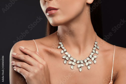Beautiful young woman with elegant jewelry on dark background, closeup