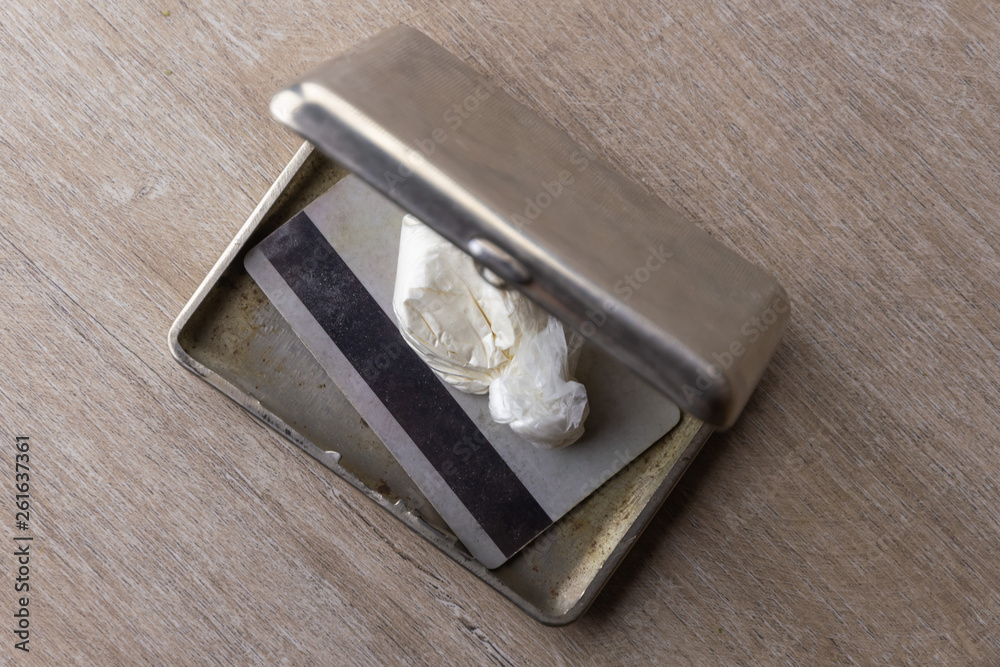 The dose of cocaine in a plastic bag and a card inside an open old cigarette case, top view The dose of cocaine in a plastic bag and a card inside an open old cigarette case, top view