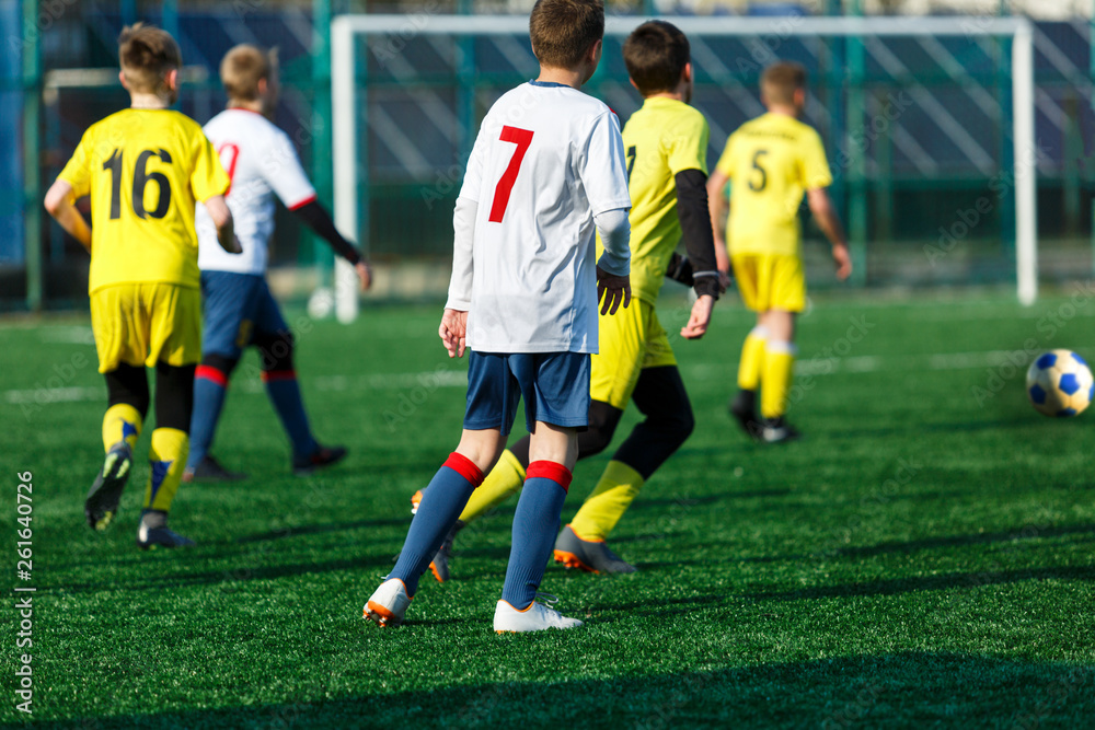 Boys in yellow white sportswear running on soccer field. Young footballers dribble and kick football ball in game. Training, active lifestyle, sport, children activity concept 