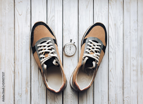 Beige sport shoes (sneakers) from suede with stopwatch on white rustic wooden background. Training, jog and sport concept. Close up, top view.