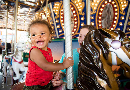 Cute mixed race little boy enjoying a ride on a fun carnival carousel. A happy boy Smiling and having fun riding a carousel ride at the summer carnival © Brocreative
