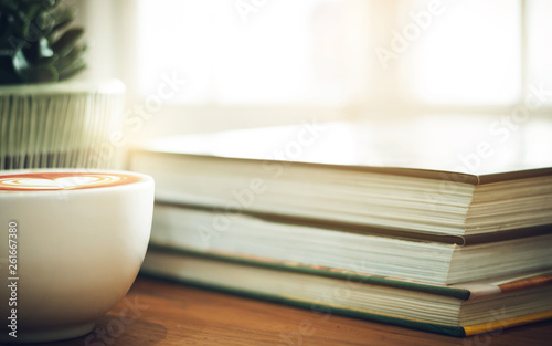 Closeup book and coffe cup on wooden table with blur small tree in ceramic vase background