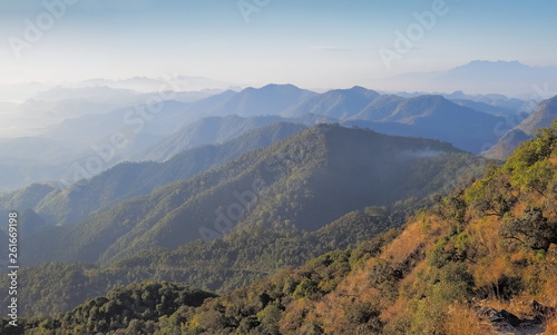 Mountain view morning on top of Doi Ang Khang above many hills and green forest cover with soft mist and blue sky background, Doi Angkhang, Chiang Mai, northern of Thailand. © Yuttana Joe