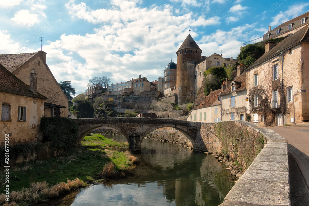 View of the ancient city of Semur-en-osua. There is a quay, a stone bridge, walls and towers of the castle. On both sides of the river are old houses. France. Burgundy.